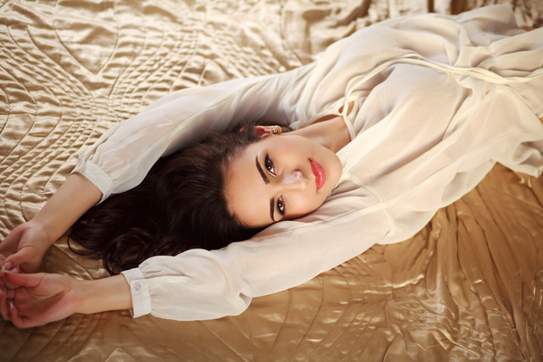 Prachtige jonge brunette vrouw ontspannen in lingerie op bed liggen  - Foto, afbeelding
