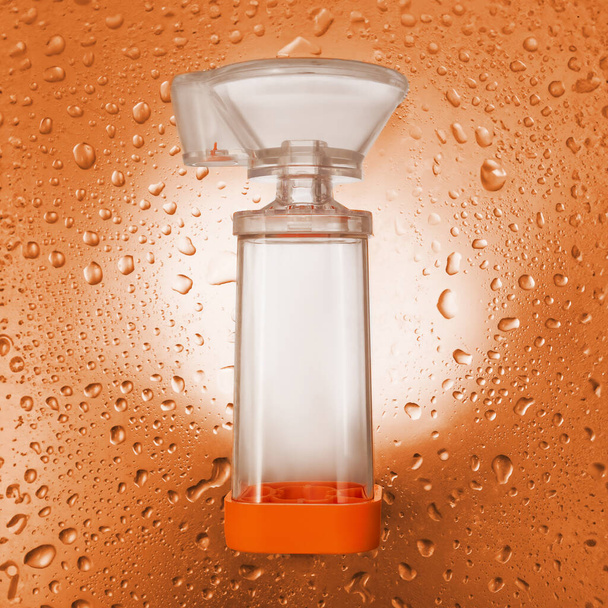 Transparent inhaler on orange background with drops. Top view - Photo, Image