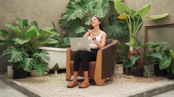 Modern fiatal nő nyújtózkodó testét, miután távolról dolgozik, vagy pihentető a magány a minimalista építészeti beton stílusú nyári egzotikus növény lombozat kert trópusi növények. Blithe! - Felvétel, videó