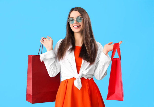Mujer joven con bolsas de compras sobre fondo azul - Foto, Imagen