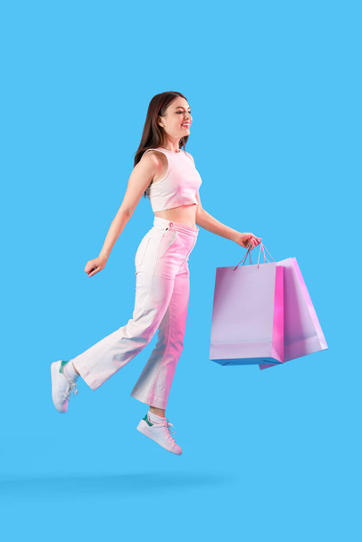 Jeune femme avec des sacs à provisions sautant sur fond bleu - Photo, image