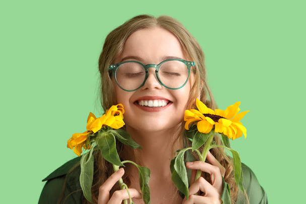 Young woman with beautiful sunflowers on green background, closeup - Zdjęcie, obraz