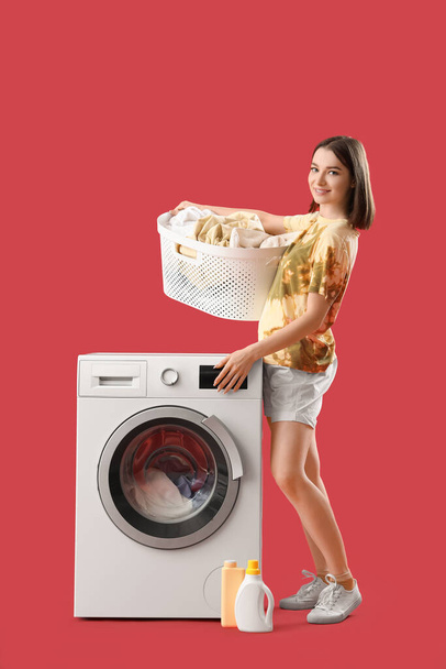 Young woman with laundry basket and washing machine on red background - Фото, изображение