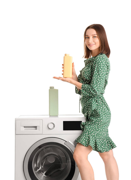 Νεαρή γυναίκα με απορρυπαντικό πλυντηρίου και πλυντήριο ρούχων σε λευκό φόντο - Φωτογραφία, εικόνα