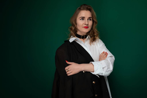A woman wearing a white shirt and black cape stands confidently. Her outfit contrasts with the background, making her stand out. The cape flows behind her, adding a dynamic element to the scene. - Photo, Image