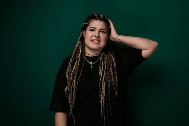 A woman with dreadlocks is standing upright in front of a solid green background. Her hair is styled in long, thin braids, and she is looking directly at the camera. - Photo, Image