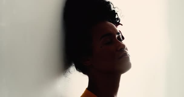 Μια σκεπτική νεαρή μαύρη γυναίκα με τα μάτια κλειστά γέρνει στον τοίχο με στοχαστική στοχαστική έκφραση. 20s Βραζιλιάνος άνθρωπος αφρικανικής καταγωγής σε ήσυχη μοναξιά - Πλάνα, βίντεο