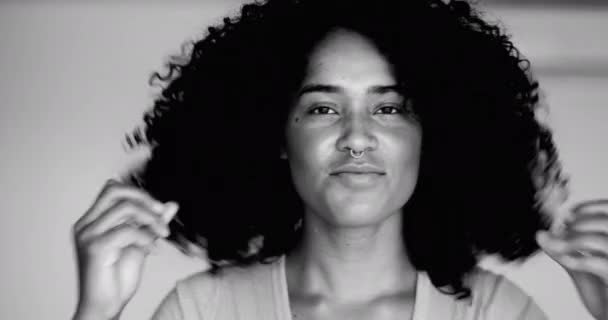 Young Brazilian black latina woman of African descent plays with curly hairstyle in monochromatic, black and white. Portrait of female 20s person getting ready adjusting hairstyle - Footage, Video