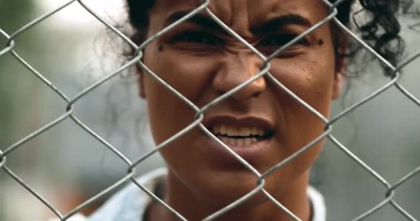 Una giovane donna nera sconvolta che urlava dietro una barriera di recinzione metallica guardando una telecamera che sghignazzava di rabbia e urlava disperata. 20s persona si sente indignato - Filmati, video