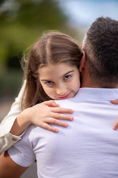 Mladá dívka pevně objímá svého otce a dívá se do kamery. ošidný pohled - Fotografie, Obrázek