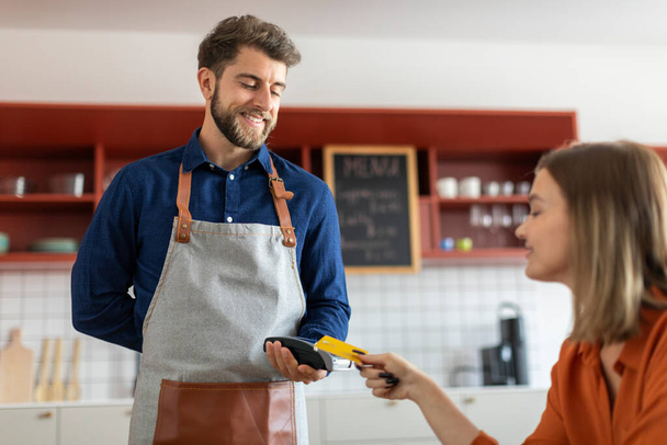 Kundin bezahlt ihre Rechnung mit NFC-Technologie und scannt ihre Kreditkarte am Zahlungsterminal, um die Transaktion im Café abzuschließen - Foto, Bild