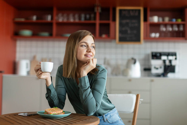 Klidná dáma s šálkem kávy v kavárně, pohled stranou na okno a snění, těší ráno nebo přestávka, volný prostor - Fotografie, Obrázek