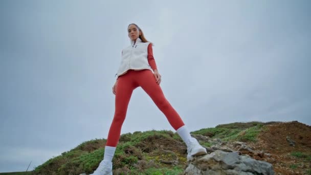 Sporty girl posing at cloudy landscape bottom view. Slim beautiful woman standing under gray gloomy sky exuding confidence and determination. Strong athlete enjoy sport routine radiating strength. - Footage, Video