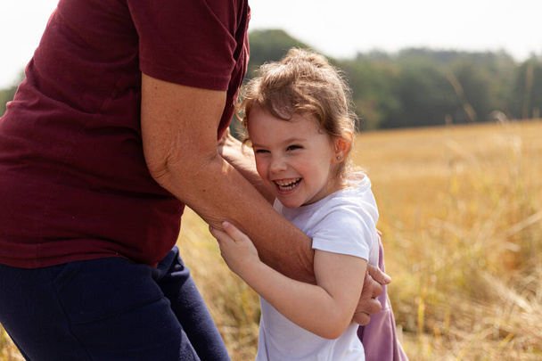 Прекрасная связь между маленькой девочкой и ее бабушкой посреди природы, празднующей радость, любовь и единение на фоне золотого пшеничного поля - Фото, изображение