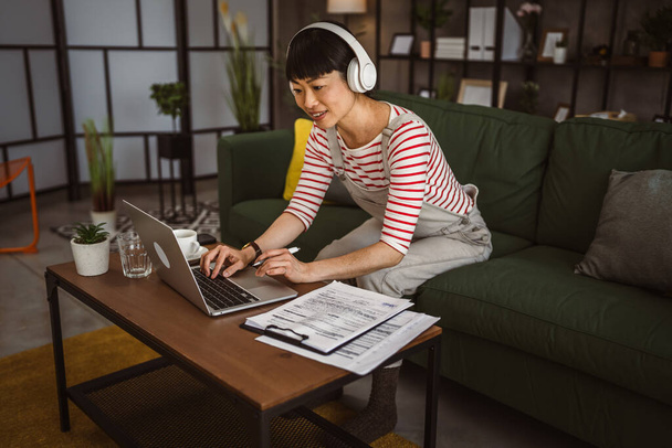 Japanse vrouw werken thuis op laptop en houd document - Foto, afbeelding