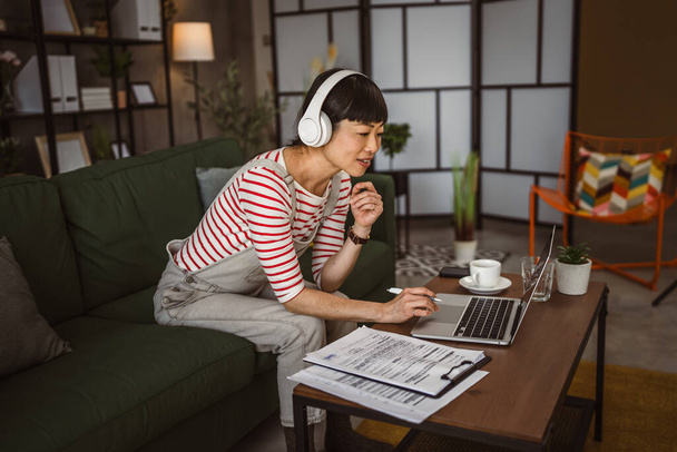 Japon kadın evde dizüstü bilgisayarda çalışıyor ve belgeyi tutuyor - Fotoğraf, Görsel