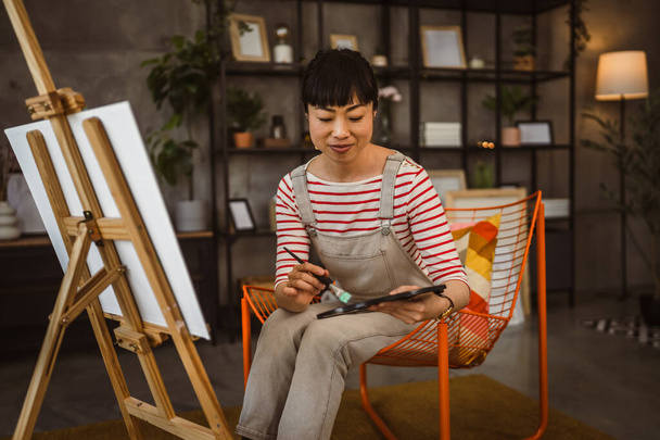 una mujer artista femenina pintar lienzo en caballete mantenga el pincel en casa - Foto, Imagen