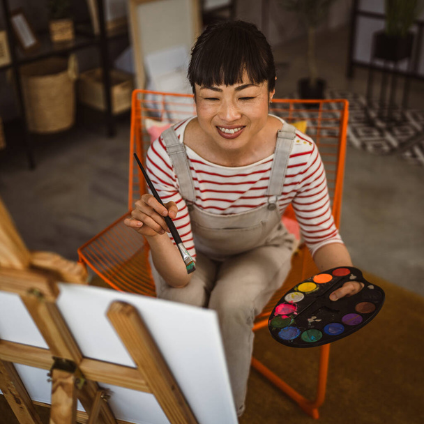 egy női művész festék vászon festőállványon tartsa ecset otthon - Fotó, kép