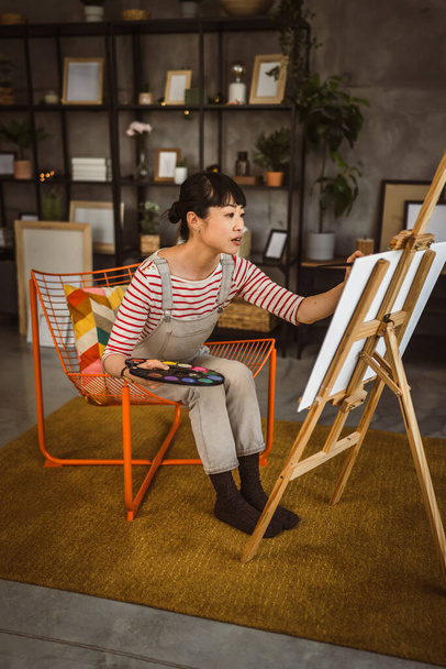 una mujer artista femenina pintar lienzo en caballete mantenga el pincel en casa - Foto, imagen