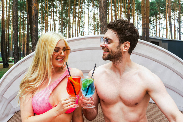 Glückliches verliebtes Paar genießt den Rest auf der Liege am Pool, während es mit Cocktails anstößt. Sommerurlaub, Beziehung, Lifestyle-Konzept - Foto, Bild