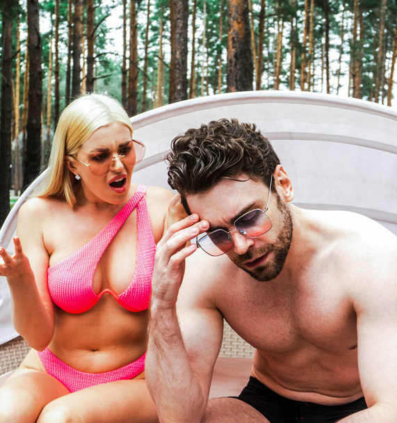 Молодая женщина устраивает скандал со своим парнем, сидя на шезлонге возле бассейна. Летние каникулы, отношения, образ жизни - Фото, изображение