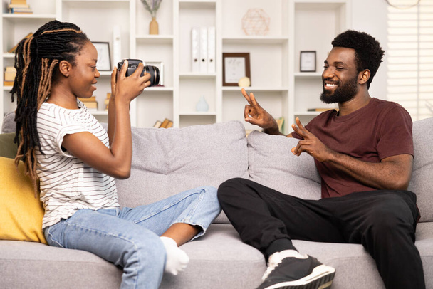 Happy African American Couple Enjoying Time At Home, Woman Taking Photos With Camera, Man Posing With Peace Sign, Casual Lifestyle, Living Room Fun Moment, Young Love, Togetherness - Fotoğraf, Görsel
