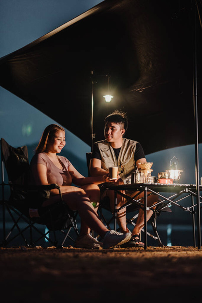 Scène tranquille d'un couple dans un camping, engageant un chat détendu à la lumière d'une lanterne suspendue le soir. - Photo, image