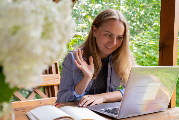 Młoda kobieta freelancer pracuje online za pomocą laptopa i korzystających z pięknej przyrody na świeżym powietrzu w ogrodzie. Internetowa edukacja spotkań. Worcation, praca z wakacji, hybrydowy model pracy - Zdjęcie, obraz