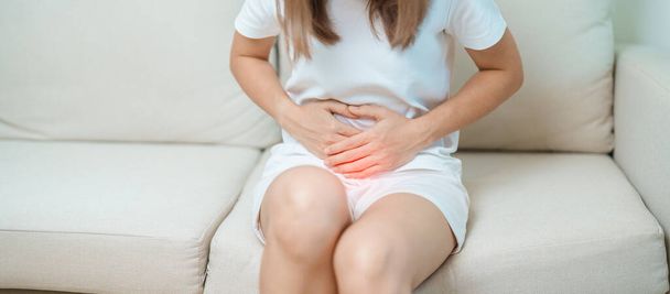 woman having abdomen ache due to Stomach pain, digestion with constipation or Diarrhea from food poisoning, female problem and Endometriosis, Hysterectomy, Stomachache and Menstrual on sofa at home - Photo, Image