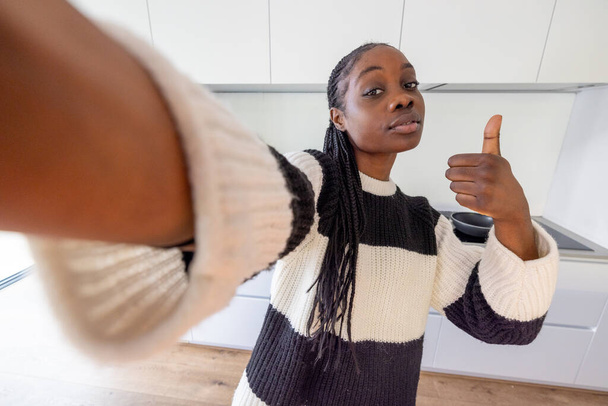 This is an engaging selfie of a confident woman in a stylish striped sweater giving a thumbs-up to the camera. The wide-angle perspective creates a dynamic feel, placing the viewer in her intimate - Photo, Image