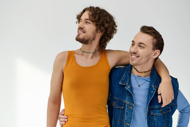 attractive merry lgbt friends in vivid attires looking at each other on gray backdrop, pride month - 写真・画像