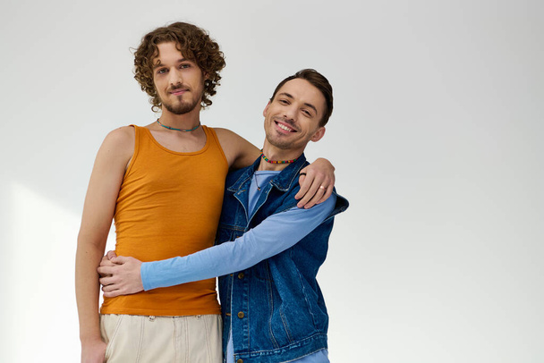 positive good looking lgbtq friends in stylish outfits posing on gray backdrop and looking at camera - Photo, image