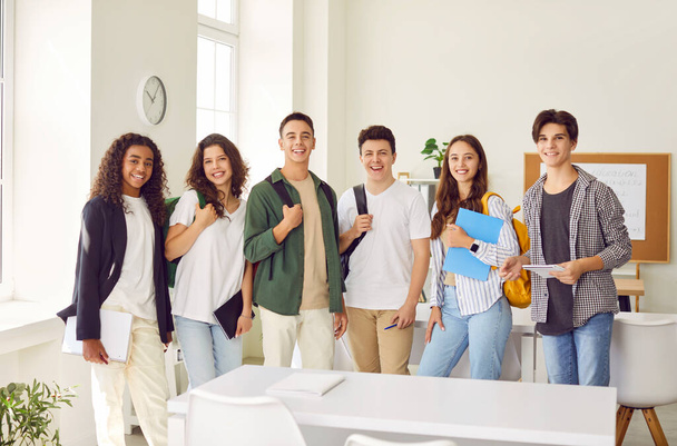 Портрет щасливої групи старшокласників, що виглядає весело на камеру і посміхається стоячи в класі. Хлопці та дівчата з рюкзаками на плечах стоять поспіль. Повернутися до концепції школи. - Фото, зображення