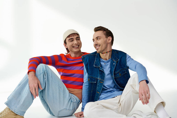 dwóch wesołych młodych przyjaciół Igbtq w żywe stylowe ubrania pozowanie razem na szarym tle - Zdjęcie, obraz