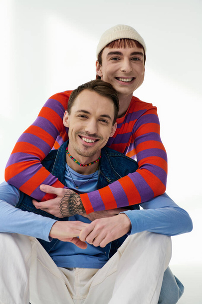 két boldog jóképű lgbt barátok élénk öltözékben nézi kamera pózol szürke háttér - Fotó, kép