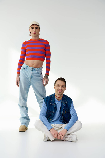 two joyous stylish lgbt friends in vibrant attires looking at camera and posing on gray backdrop - Foto, imagen