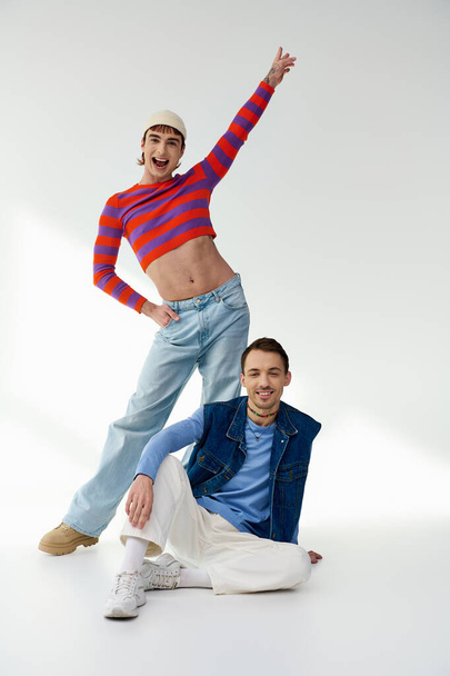 two happy appealing lgbt friends in vibrant attires looking at camera and posing on gray backdrop - Photo, Image