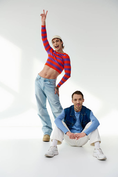 two jolly appealing lgbt friends in vibrant attires looking at camera and posing on gray backdrop - Fotoğraf, Görsel