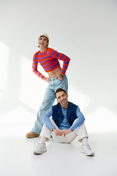 two merry trendy lgbt friends in vibrant attires looking at camera and posing on gray backdrop - Foto, imagen