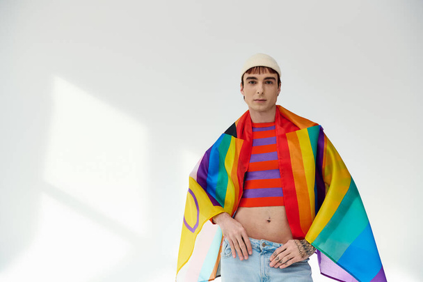 alegre bonito gay homem no vívido roupa com branco chapéu segurando arco-íris bandeira e olhando para câmera - Foto, Imagem