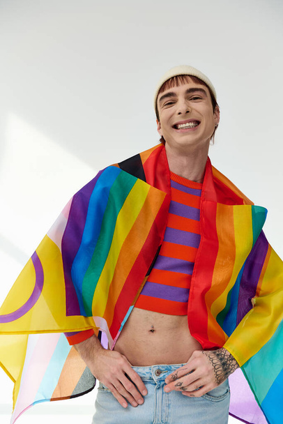 schöner lustiger schwuler Mann in lebendigem Outfit mit weißem Hut mit Regenbogenfahne und Blick in die Kamera - Foto, Bild