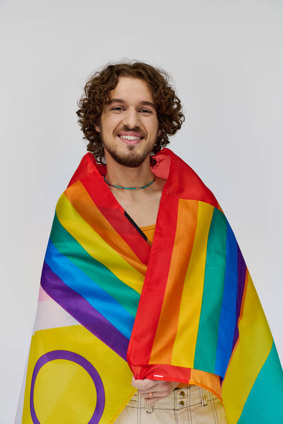 joyeux séduisant gay homme avec les cheveux noirs tenant drapeau arc-en-ciel et souriant heureux à la caméra - Photo, image
