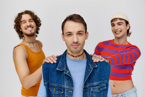 vrolijk knap gay mannen in vibrant attires poseren samen op grijs achtergrond en kijken naar camera - Foto, afbeelding