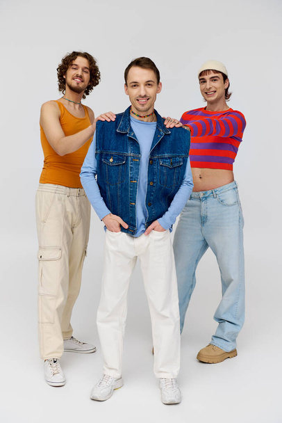 cheerful handsome gay men in vibrant attires posing together on gray backdrop and looking at camera - Fotoğraf, Görsel