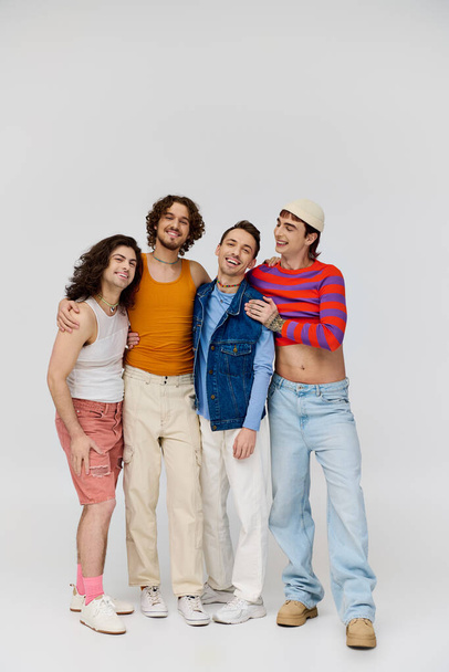 four merry good looking gay men in vivid attires smiling at camera while posing on gray backdrop - Zdjęcie, obraz