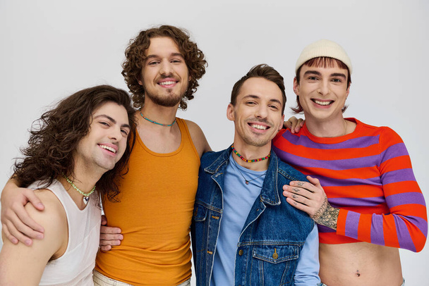 four jolly good looking gay men in vivid attires smiling at camera while posing on gray backdrop - Foto, afbeelding