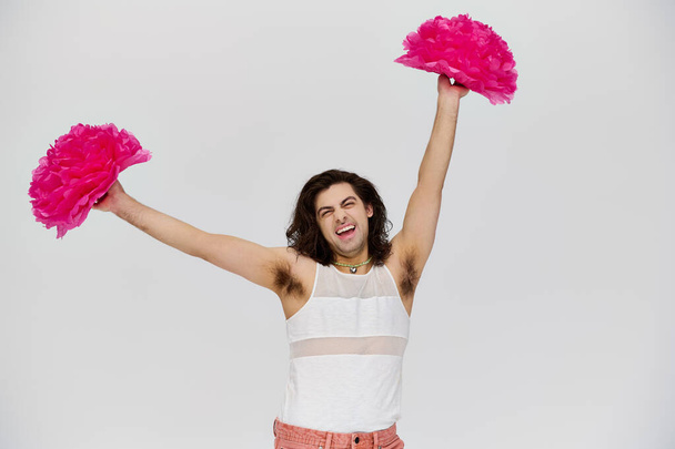 cheerful attractive gay man in vibrant attire posing happily with pom poms and smiling at camera - Photo, Image