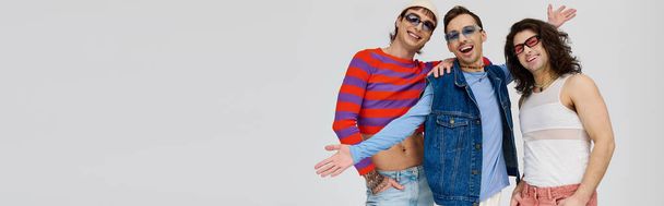 três chique atraente gay amigos no vibrante moda trajes com óculos de sol, orgulho mês, banner - Foto, Imagem
