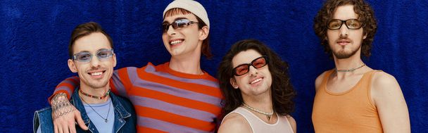 joyeux beaux hommes gays avec des lunettes de soleil dans des vêtements vifs posant sur fond bleu, mois de fierté, bannière - Photo, image