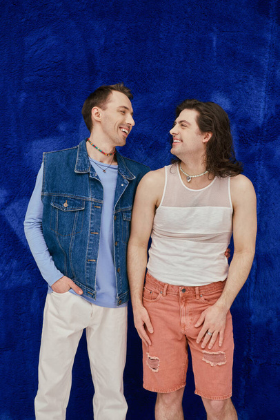 positive attractive elegant gay friends in cozy outfits on dark blue backdrop, pride month - Foto, Imagen